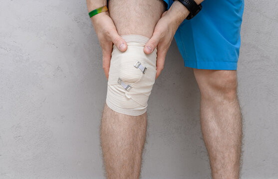 Athlete holding his bandaged knee, knee pain after injury - Powered by Adobe