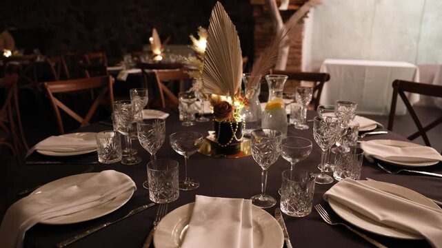Wide shot of a formal dinner table set with crystal glasses, white napkins, and a dried floral centerpiece under warm lighting. Elegant and symmetrical layout with copy space