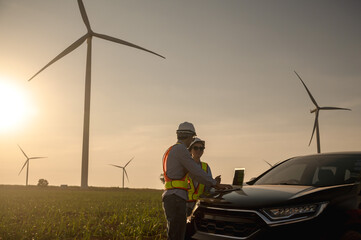 Male and female wind turbine engineers working together until sunset in wind turbine field