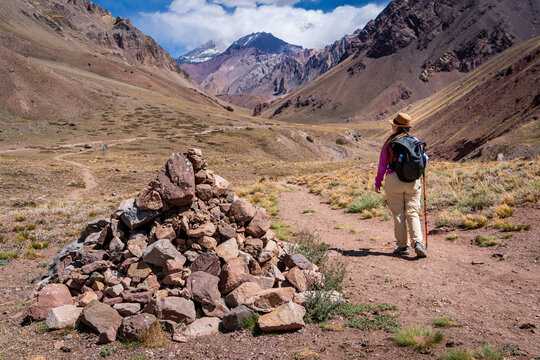 Mujer senderista recorrindo los senderos del Parque Provincial Aconcagua, pasando al lado de una t&iacute;pica selallizaci&oacute;n local de rocas, llamada apacheta.
