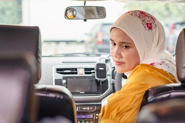 A young Indonesian Muslim woman checking her belongings in the back seat of her car before driving