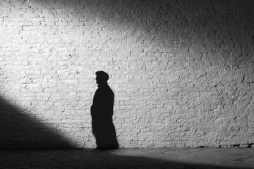 Obraz premium Silhouette of a person illuminated by a spotlight against a brick wall