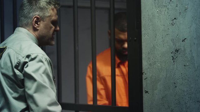 Angry prison guard escorting inmate in orange robe from cell, abuse of power