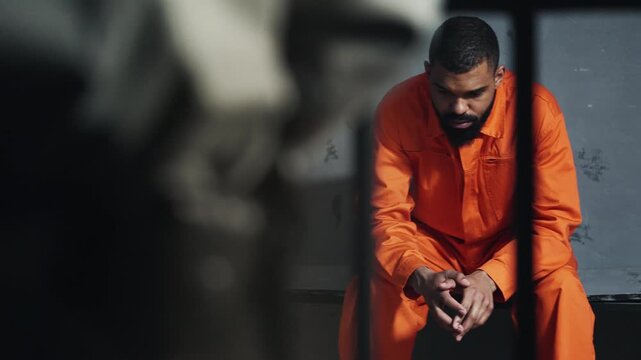 Strict prison guard controlling inmate behind bars, discipline and authority