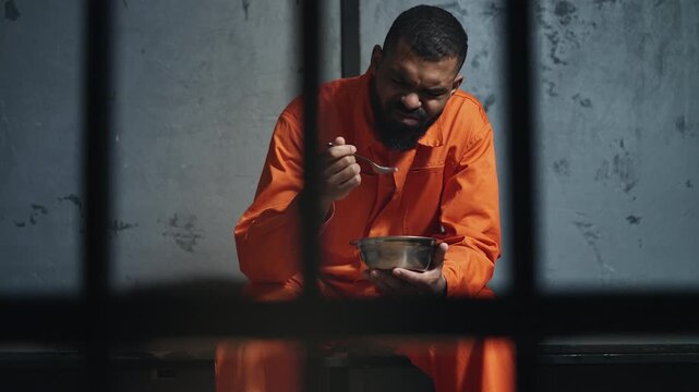 African American male prisoner eating tasteless prison food behind cell bars