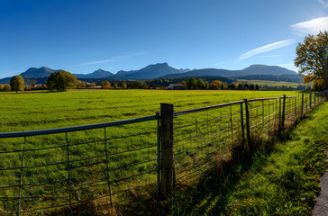 Green countryside landscape with wooden fence leading toward mountains under clear sky
