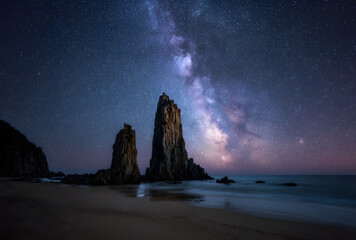 Rock formations on quiet beach under starry night sky and milky way creating dramatic cosmic landscape
