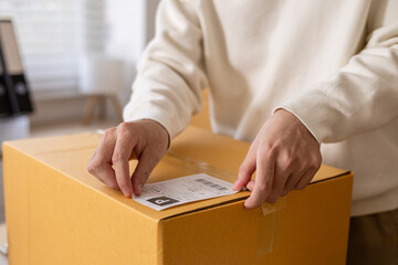 Small business warehouse scene of worker apply shipping label on parcel and taping cardboard box, organizing delivery tasks, order preparation and maintaining efficient packing workflow, multitasking