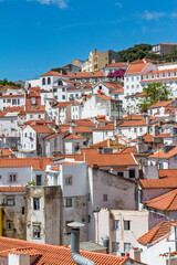 Vertical cityscape view of Lisbon's historic district, featuring traditional white buildings with terracotta red tile roofs under a blue sky.