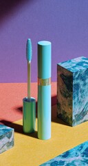 A vibrant teal mascara tube and wand are presented against a colorful backdrop of orange, purple, and yellow surfaces, accented by two blue marble blocks.  Dramatic lighting casts shadows