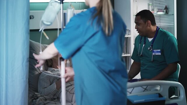 Surgeon consulting senior female patient in ICU bed while nurse placing IV drip