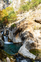 Vertical Shot of a Rocky Canyon Waterfalls Feeding an Emerald Green Natural Pool Under Bright Sunlight