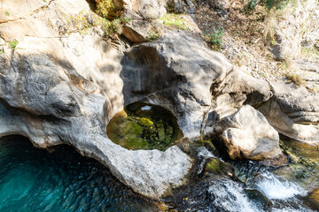 Top-Down View of a Small, Circular Natural Pool and Water-Eroded Limestone Rock Basins in a Sunny Gorge