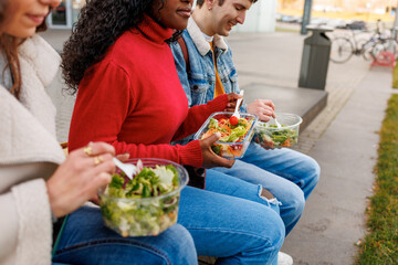 Multiethnic young students eating fresh salads together outside university