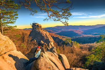 Confident woman hiker resting on mountain rocks at golden hour