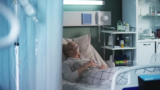 Ill senior woman in oxygen mask lying in ICU bed, receiving intensive care