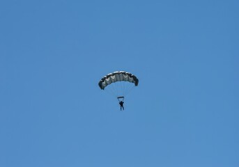 Airborne military figure descending rapidly from an aircraft high above the earth. A large parachute canopy is fully deployed against the vast blue sky ,force ,descent ,blue sky