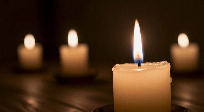 a group of four white candles on a wooden table. The candles are lit, creating a warm and inviting atmosphere. The background is dark, making the candles stand out even more