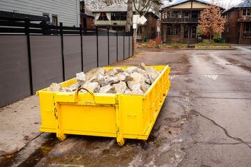 Yellow construction dumpster filled with broken concrete on a residential street in the Beaches neighbourhood, Toronto, Canada, during fall. Urban renovation and building materials in outdoor setting.