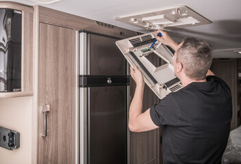 Obraz premium Man Repairs an Air Condition Appliance in Kitchen of Modern Motorhome Vehicle During Daytime Hours