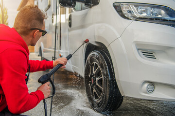 Man Washes a Camper Van RV With a Pressure Washer in a Sunny Location