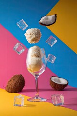 Coconut ice cream in glass with floating ice cubes and coconut slices
