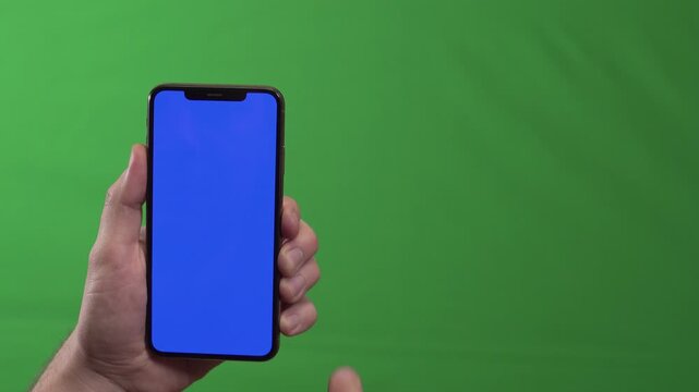 Hand holding phone with blue screen, steady grip and vertical orientation against green chroma background, high detail product mockup for interface preview,
