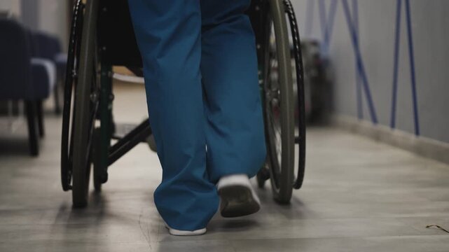 Nurse in uniform pushing wheelchair with patient through hospital corridor