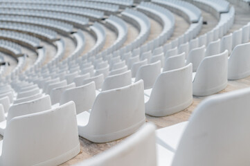Fototapeta premium Rows of empty white seats arranged in a circular pattern inside a large outdoor venue during the day