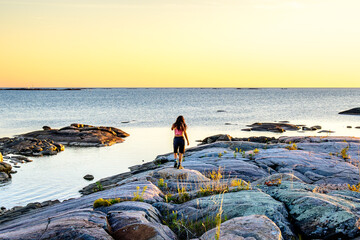 Young woman walking on exposed granite shoreline along Georgian Bay, Ontario, Canada, during fall. Coastal recreation setting associated with sea kayaking and shoreline access.