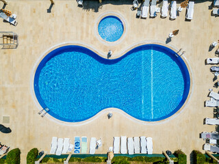 Perfectly Symmetrical Overhead Aerial View of a Figure-Eight Shaped Swimming Pool and Separate Circular Wading Pool Surrounded by Sunbeds