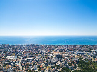 High-Altitude Drone View of a Dense Urban Area Extending Along a Beachfront, with Clear Blue Skies and Ocean Horizon