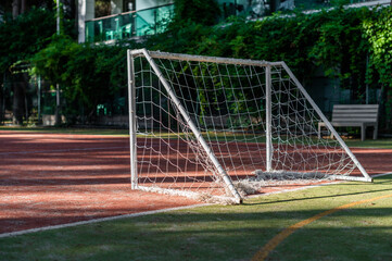 Soccer goal stands on the field surrounded by trees during the afternoon sunlight