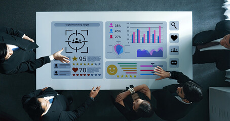 A group of professionals collaborates around a touchscreen table displaying interactive graphs and marketing metrics in a modern office environment. Gantry