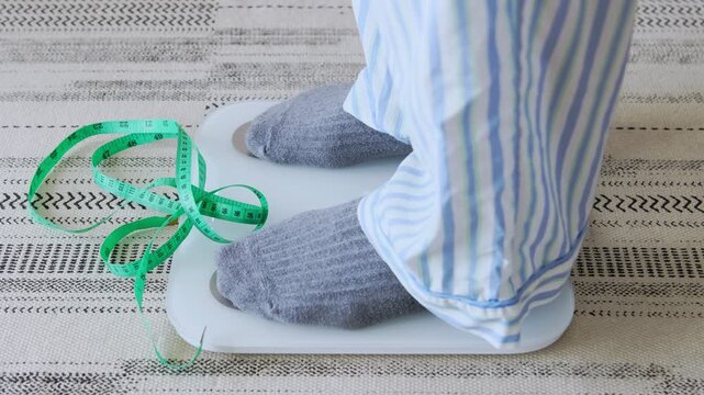 Person in pajamas steps off a weight scale with a measuring tape, achieving a weight loss goal