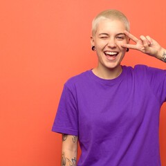 Person shows peace sign and smiles in front of orange wall