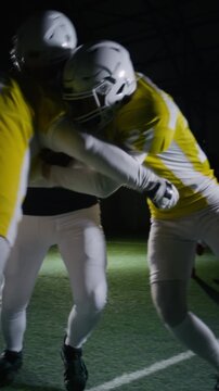 Vertical shot of young Caucasian male American football cornerback in blue jersey catching ball and getting intercepted by players in yellow uniform from rival team during championship match