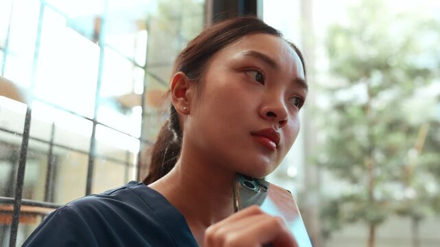 Sad female medical professional looking worried and pensive while holding a phone. Young nurse feeling stressed after a tough shift