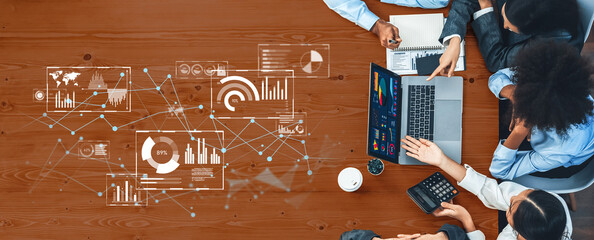 A view from above of a business team collaborating on a project, analyzing data and charts displayed on a laptop in a modern office environment. Trope