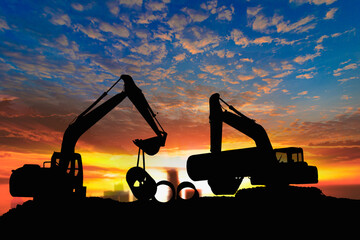 Two Crawler Excavator silhouette is digging soil in  construction site with  pipeline work on sunset backgrounds.