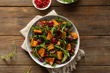 Fresh salad with roasted pumpkin and grapes on plate wooden surface