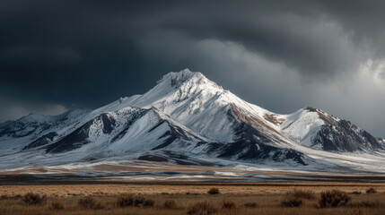 Majestic snow capped mountain peak rises dramatically under an ominous dark sky showcasing a scenic landscape on a vast plain in a remote wilderness area.