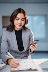 Asian businesswoman analyzing financial report using smartphone