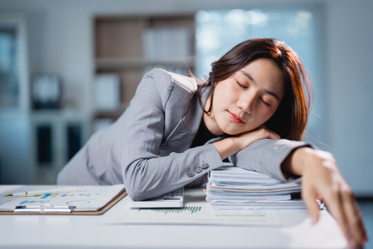 Asian businesswoman sleeping on desk feeling exhausted and overworked
