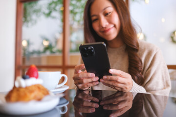 Portrait image of a woman holding and using mobile phone with coffee cup and cake on the table in cafe