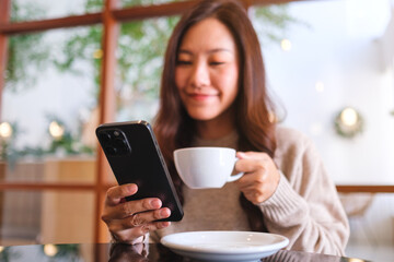 Portrait image of a woman holding and using mobile phone while drinking coffee in cafe