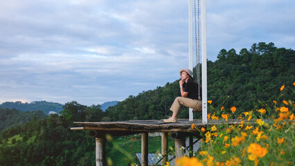 Portrait image of a woman sitting on a swing with a beautiful flower garden and mountain on cloudy day