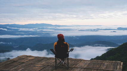 Rear view of a woman sitting and looking at a beautiful foggy mountain before sunrise