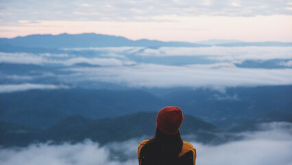 Rear view of a woman sitting and looking at a beautiful foggy mountain before sunrise