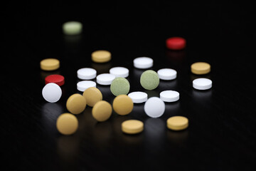 Pills scattered on a black wooden table. Background for pharmacy, antibiotics, vitamins, dietary supplements